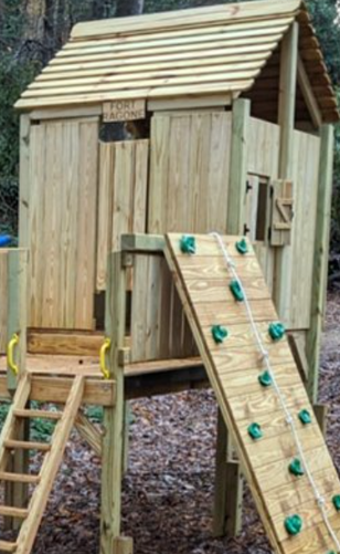 Wooden backyard playhouse with a slanted roof, rope ladder, and climbing ramp with green holds
