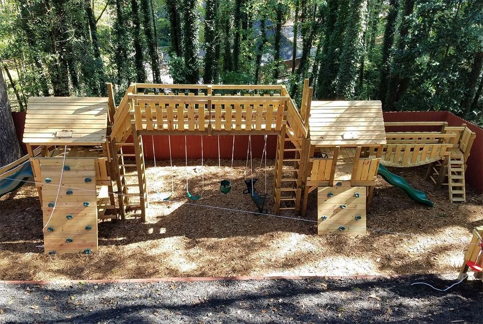 Wooden playground fort with bridges and slides in a wooded outdoor setting