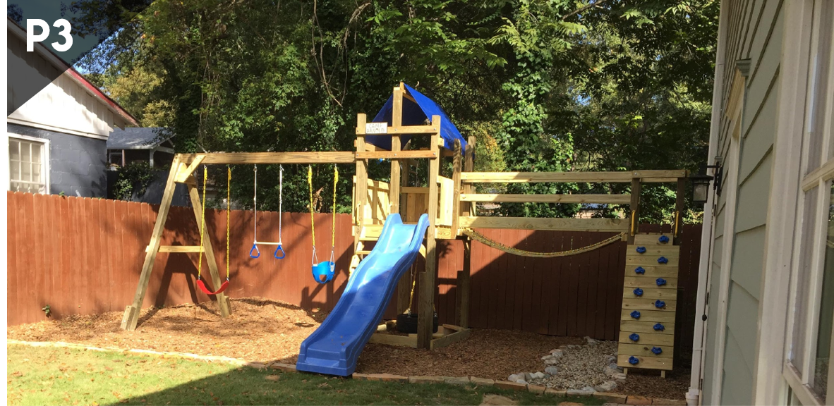 Backyard playground with blue slide, swings, and climbing structure beside a house and wooden fence