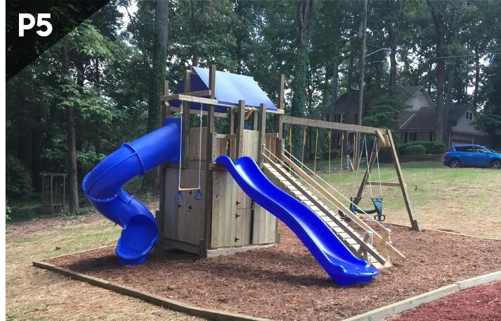 Playground with blue slides, swings, and a climbing structure in a wooded park