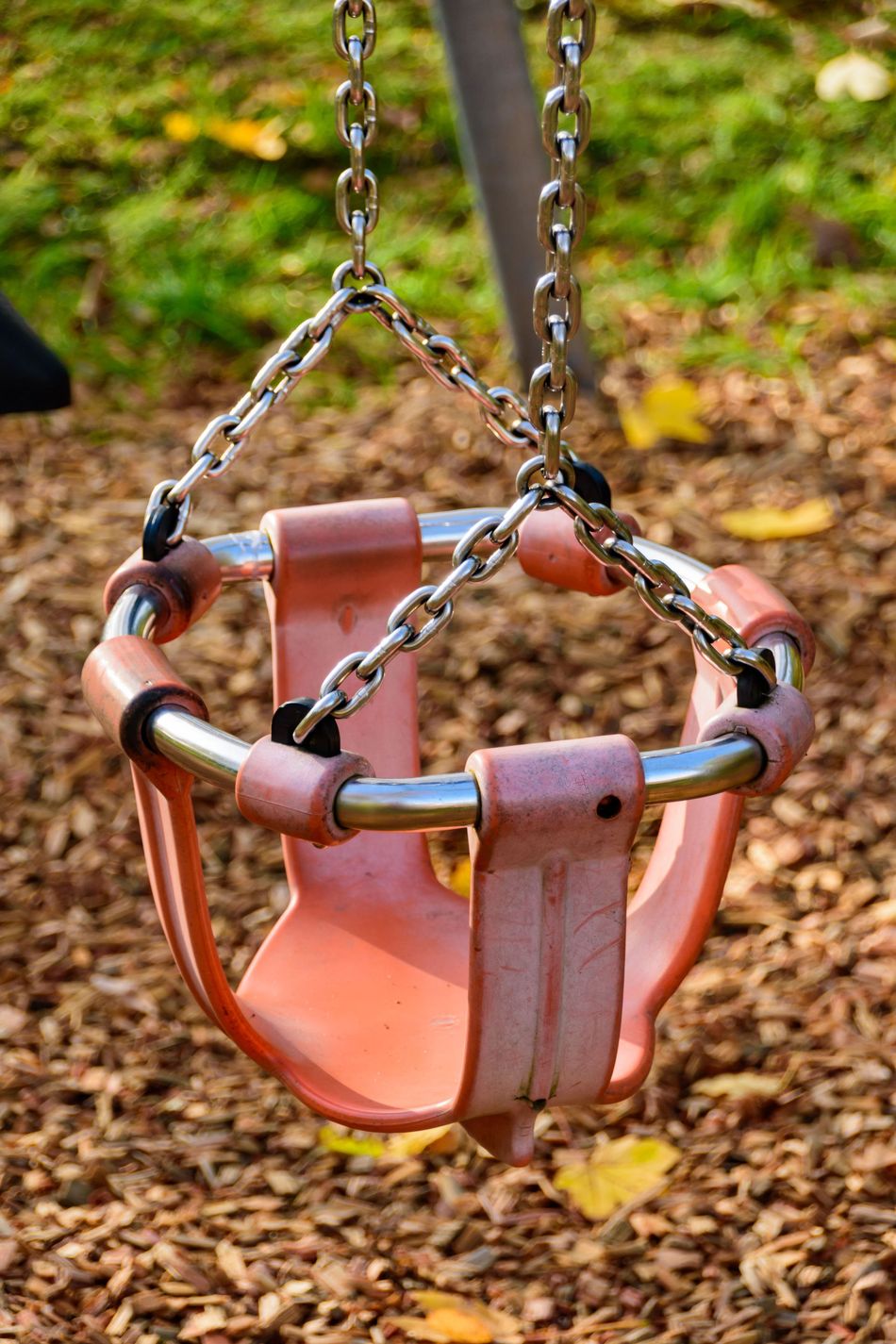 Pink toddler swing seat hanging from chains over wood chips in a playground