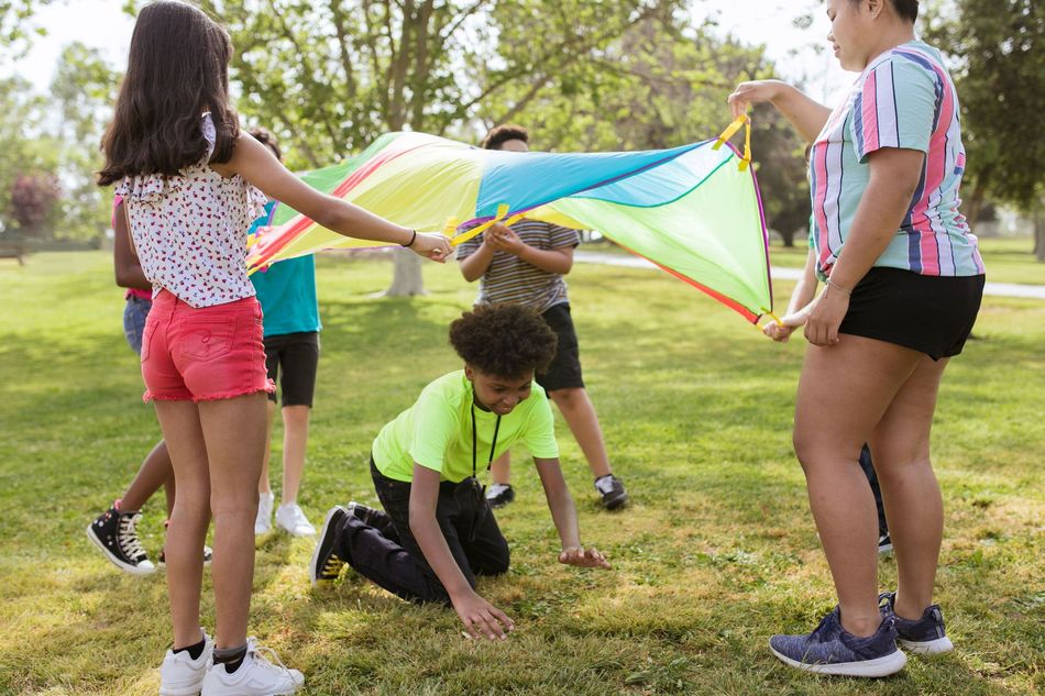 Children playing under a colorful parachute in a grassy park