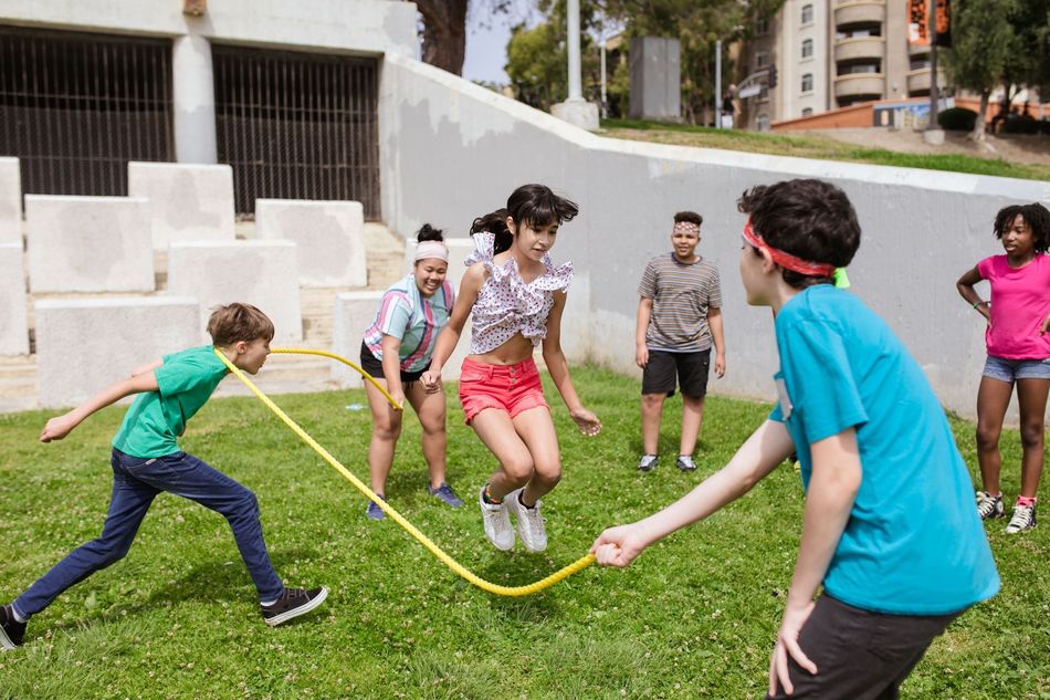Children playing tug-of-war on a grassy lawn with a yellow rope outdoors.