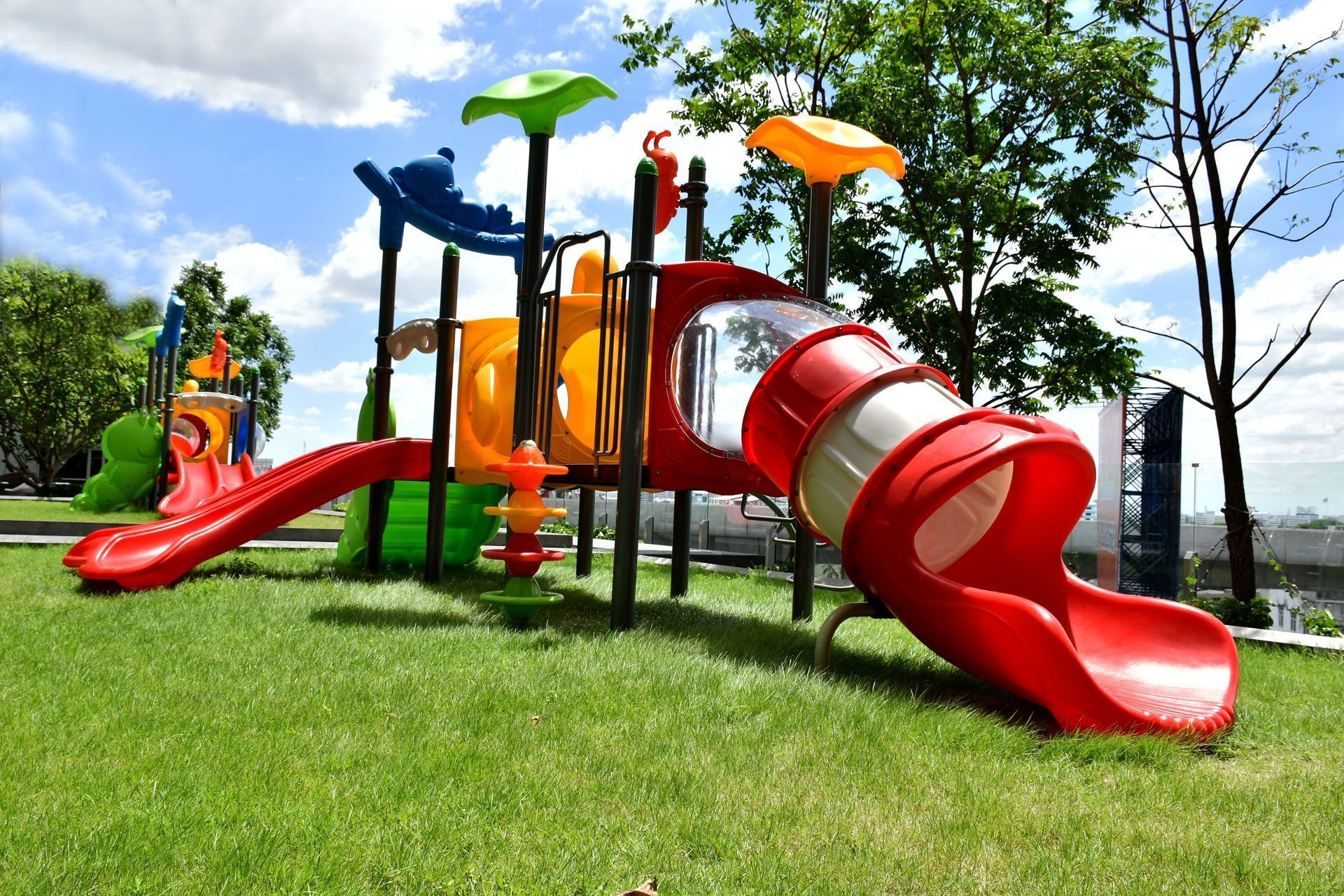 Colorful playground with red slides, orange and green play towers, and grassy park surroundings