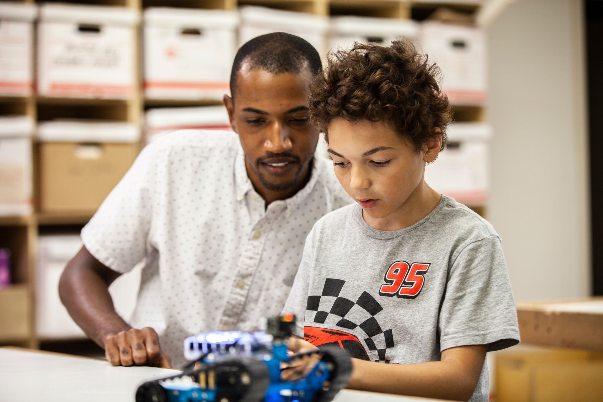 A Big and Little working together on a small robotics project at a table, focused on the device.