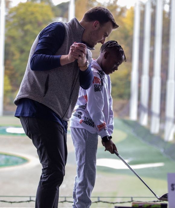 Big and Little golfing together at a driving range at Top Golf for a fundraiser, holding clubs and preparing to swing