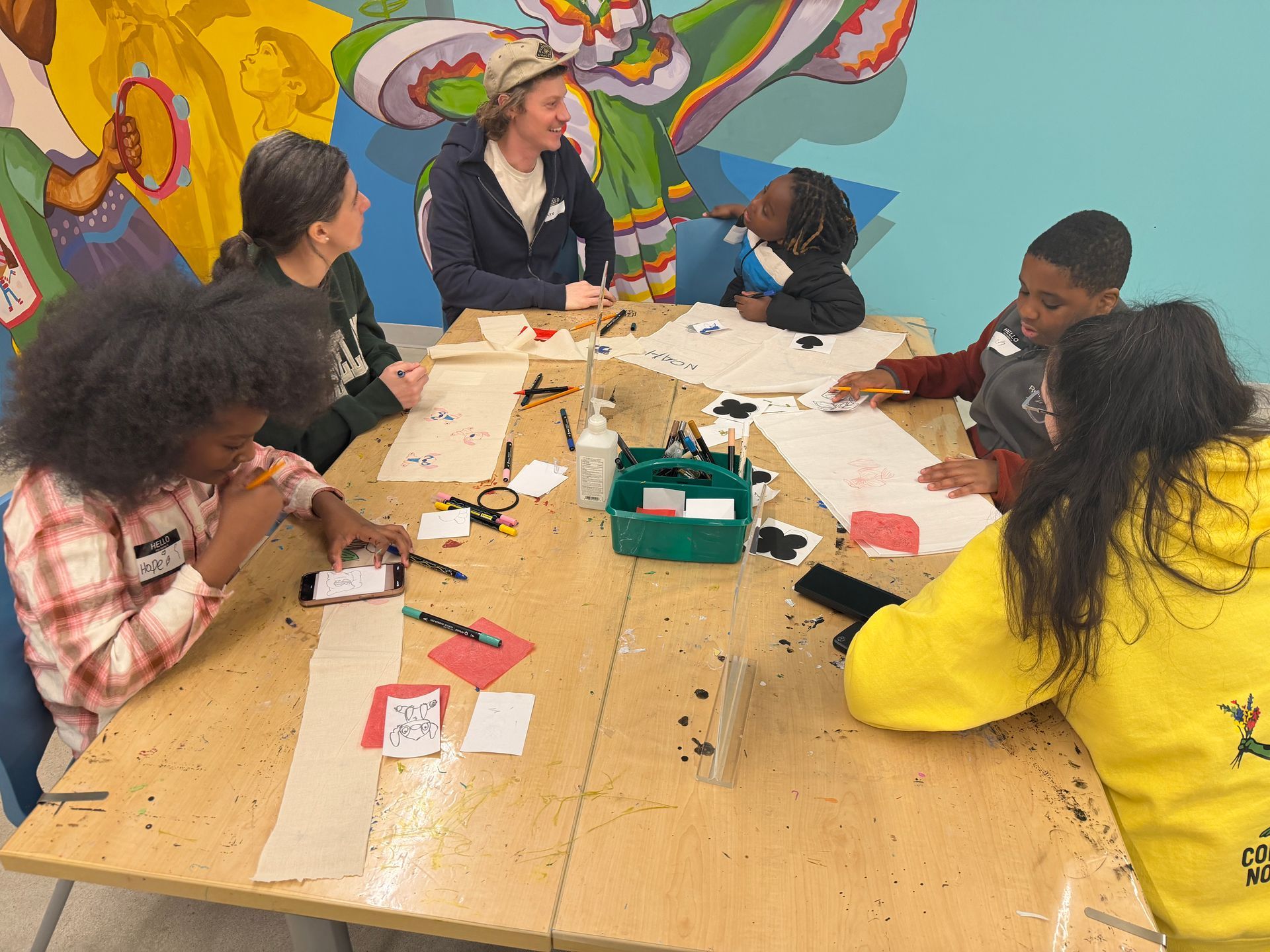 Bigs and Littles gathered around a craft table in a colorful classroom, making art together.