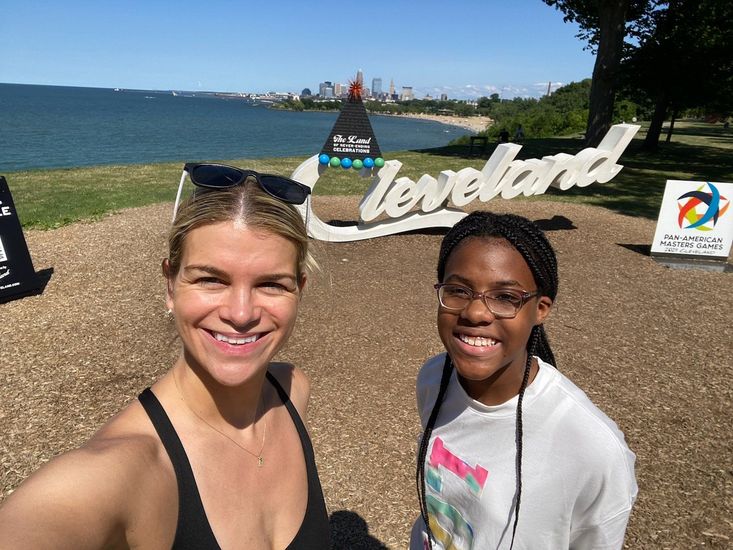 A Big and Little smiling people posing by a Cleveland waterfront sign on a sunny day