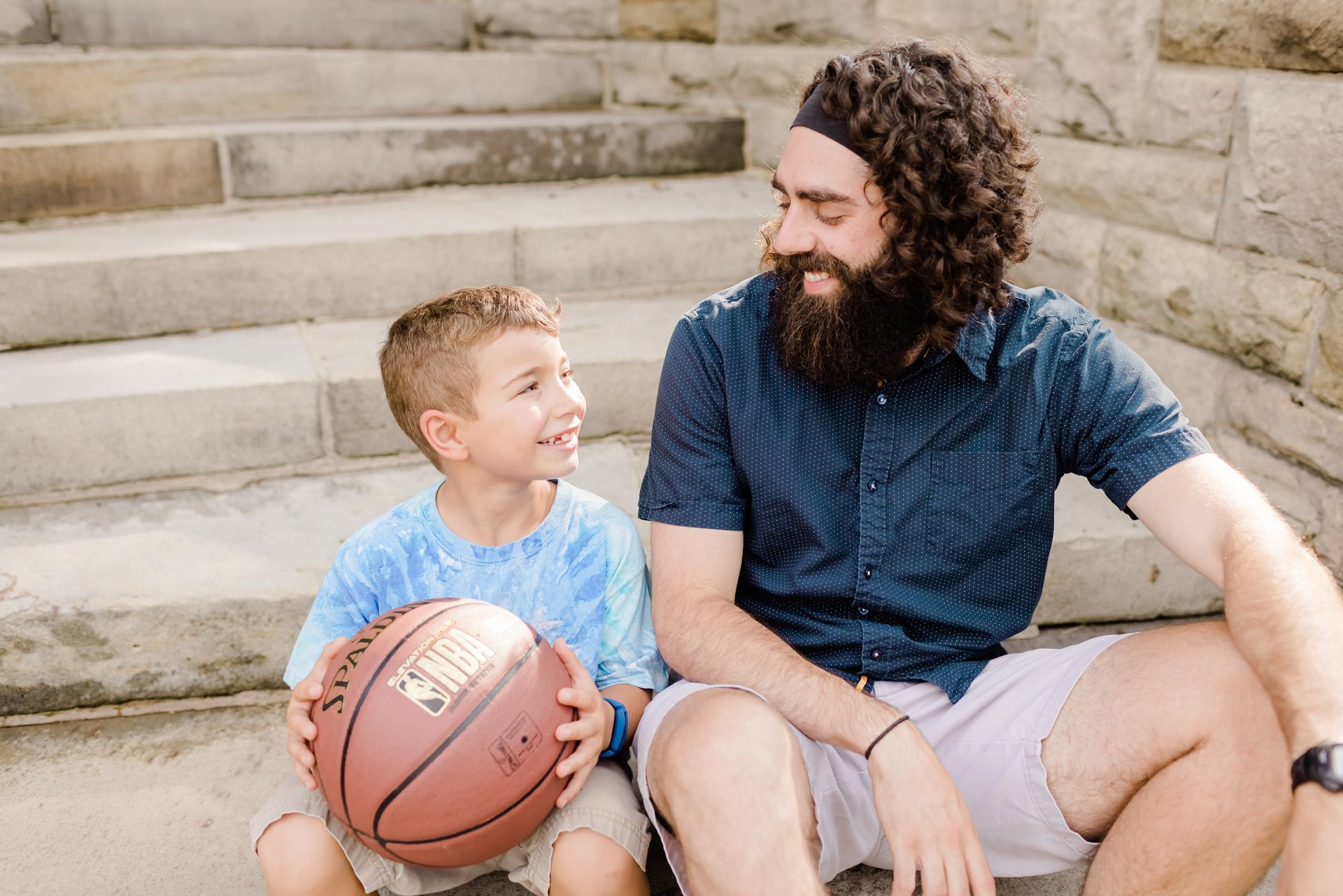 A Big Brother and Little Brother sitting on steps, smiling and holding a basketball