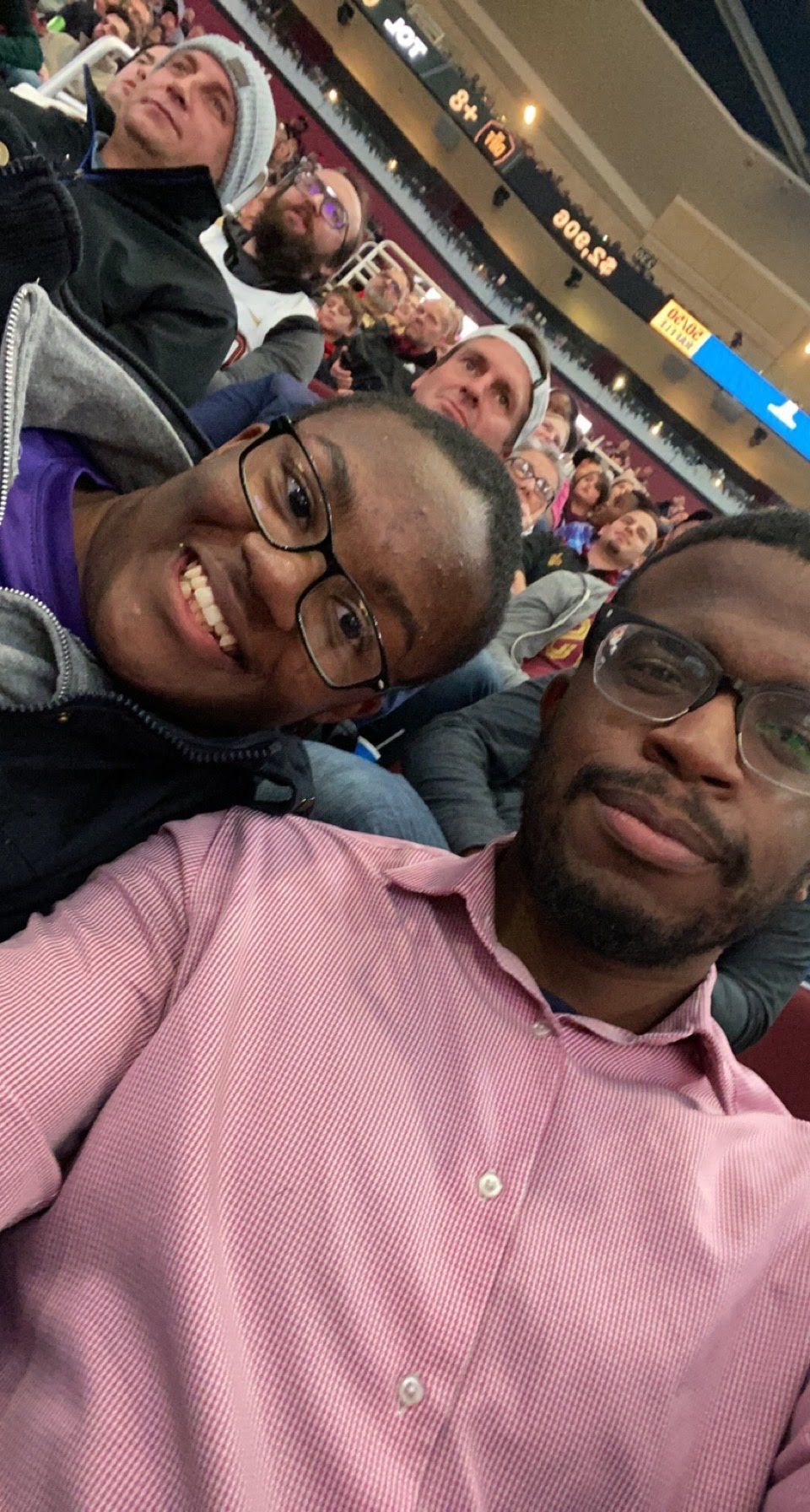 Big and Little taking a selfie in a stadium crowd, one in a pink shirt and one in glasses.