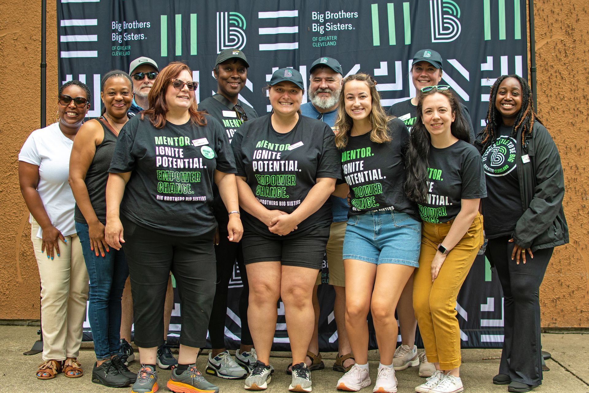 Big Brothers Big Sisters of Greater Cleveland staff and board posing outdoors in front of a branded backdrop, smiling and wearing matching event T-shirts
