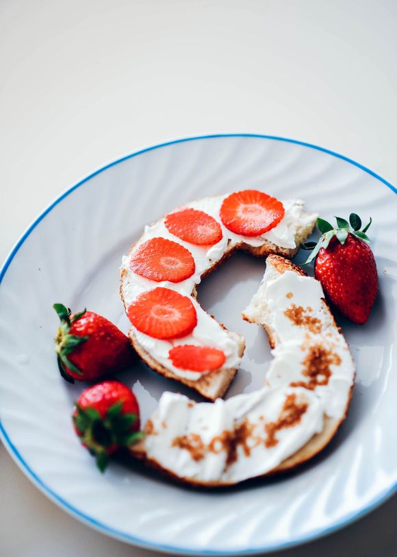 White plate with sliced strawberries arranged as a crescent on a cream dessert, with whole strawberries рядом