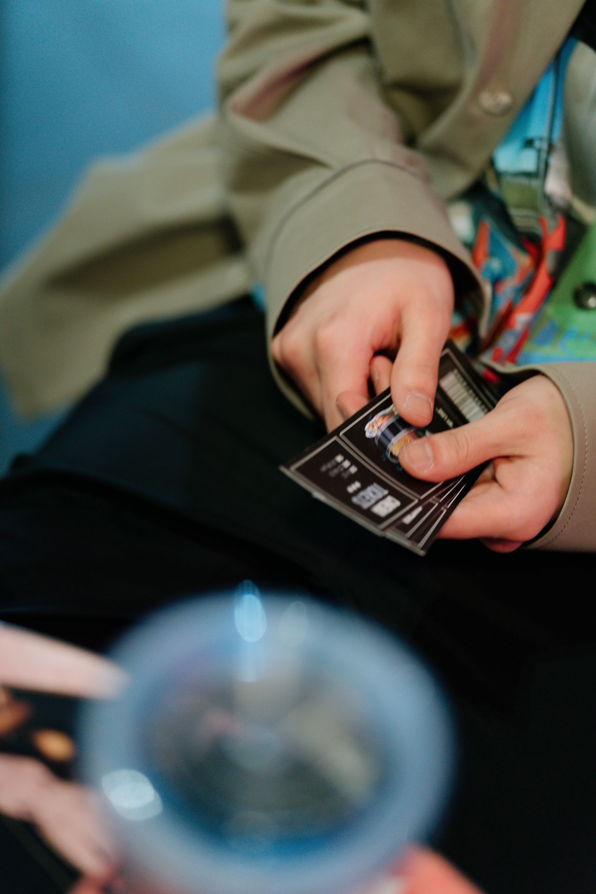 Hands holding tickets over a lap, with a blurred cup in the foreground.