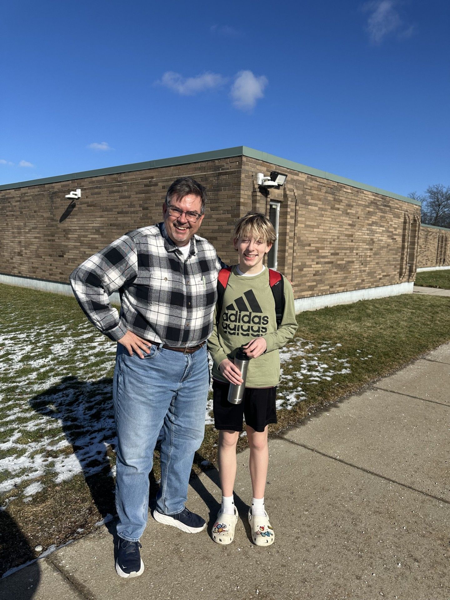 A Big Brother and posing on a sidewalk beside a brick building under a sunny blue sky.