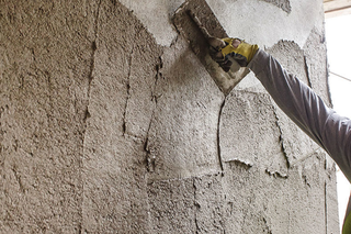 Person applying plaster to a wall with a trowel.