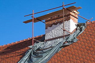 Chimney on a red tiled roof being repaired, scaffolding and tarp present.