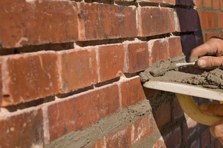 A person uses a trowel to apply mortar between red bricks, repairing a wall.