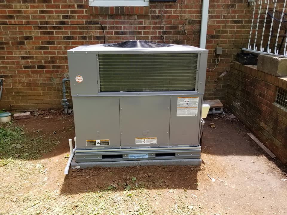 A large air conditioner is sitting outside of a brick building.