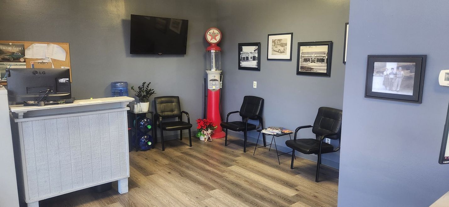 A small waiting room with a reception desk, three chairs, a vintage gas pump, and framed photos on blue-gray walls.
