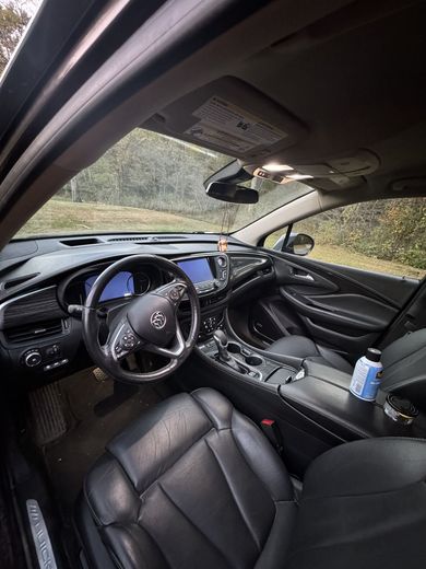 The interior of a Buick car features black leather seats, a dashboard with a touchscreen, and a steering wheel with a logo.