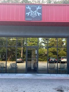 A storefront with a skull and crossed wrenches logo on a red awning above large glass doors and windows.
