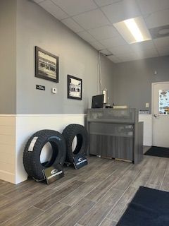 A customer service desk area with two large tires on the floor against a gray wall with two framed pictures.