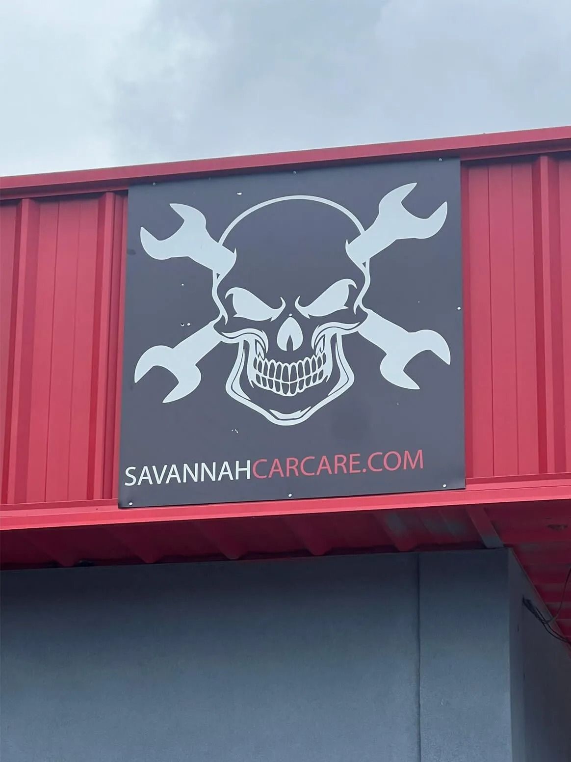 A sign with a skull and crossed wrenches logo above the text SAVANNAHCARCARE.COM on a red and gray building.