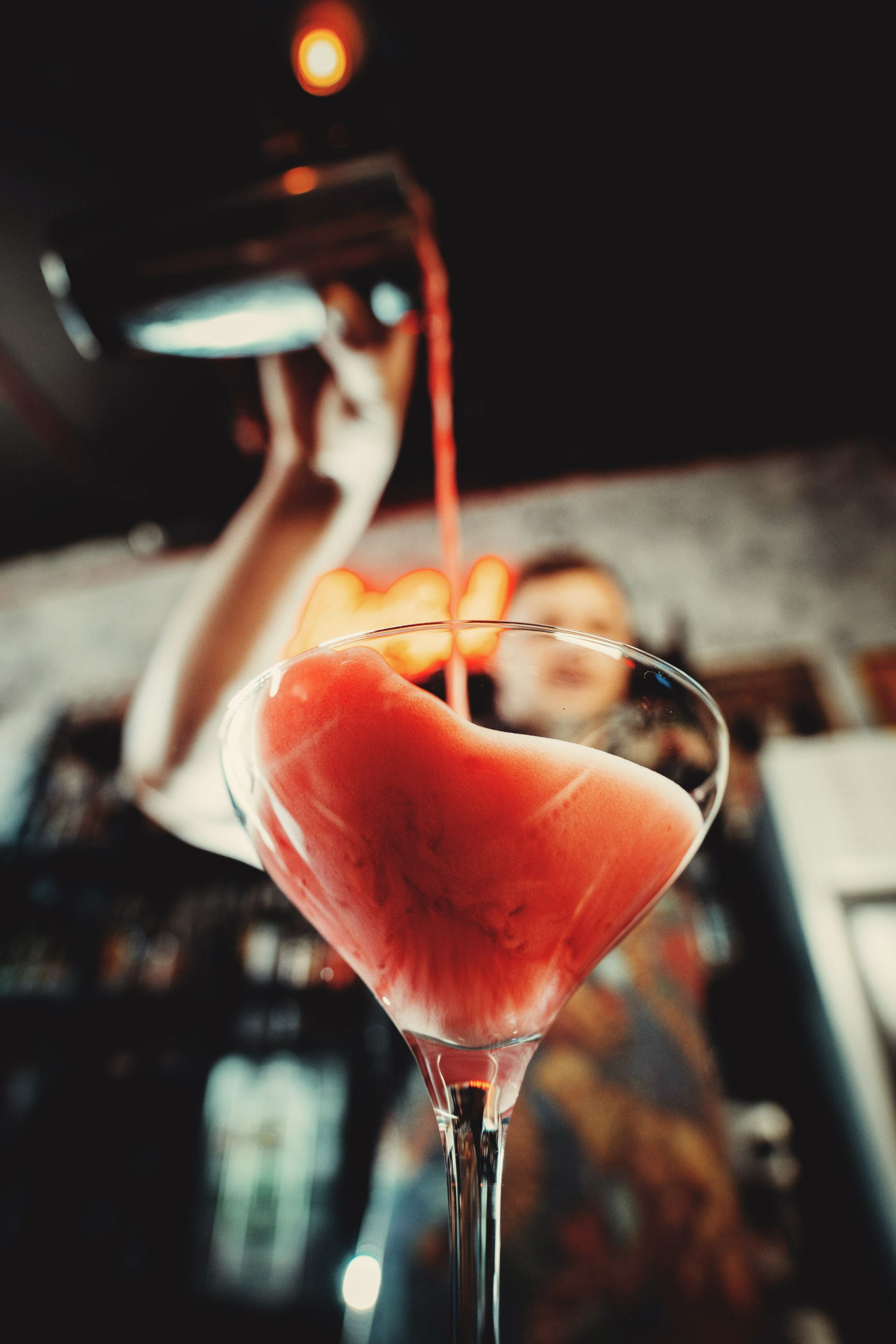 Cocktail glass with a watermelon slice garnish at a bar, with liquor being poured in the background