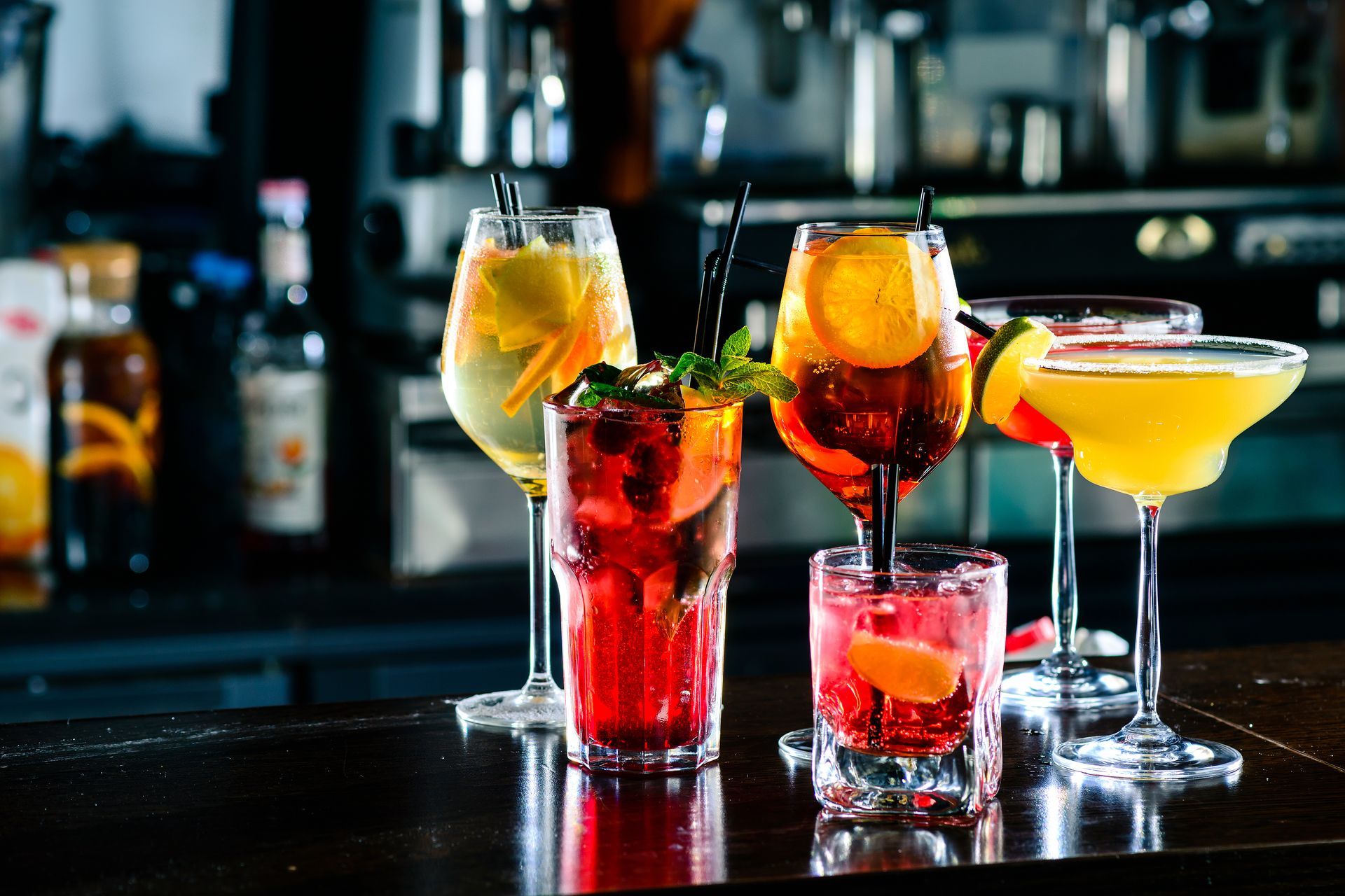Assorted colorful cocktails on a bar counter with blurred bottles in the background