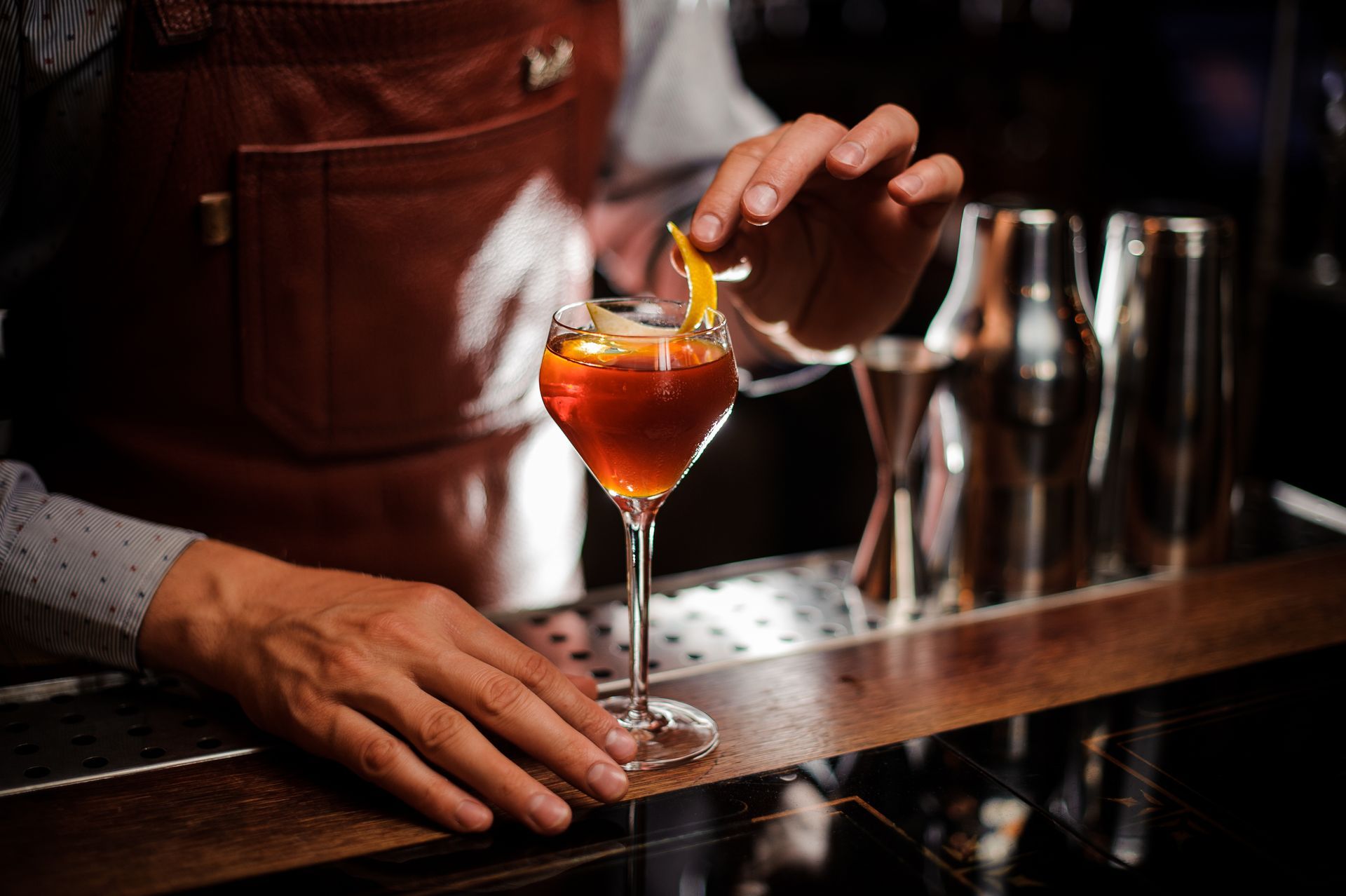 Bartender garnishing an amber cocktail at a bar with a spoon and stemmed glass