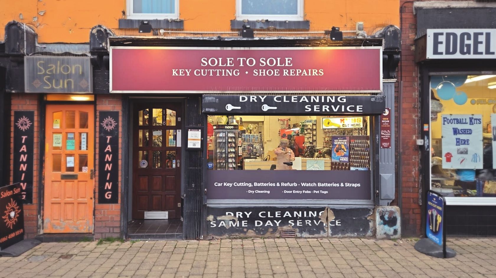 Exterior of Sole to Sole shopfront in Stockport showing garnet signage with services including key cutting, shoe repairs, dry cleaning, and engraving, with the shop’s signature animatronic cobbler in the window.