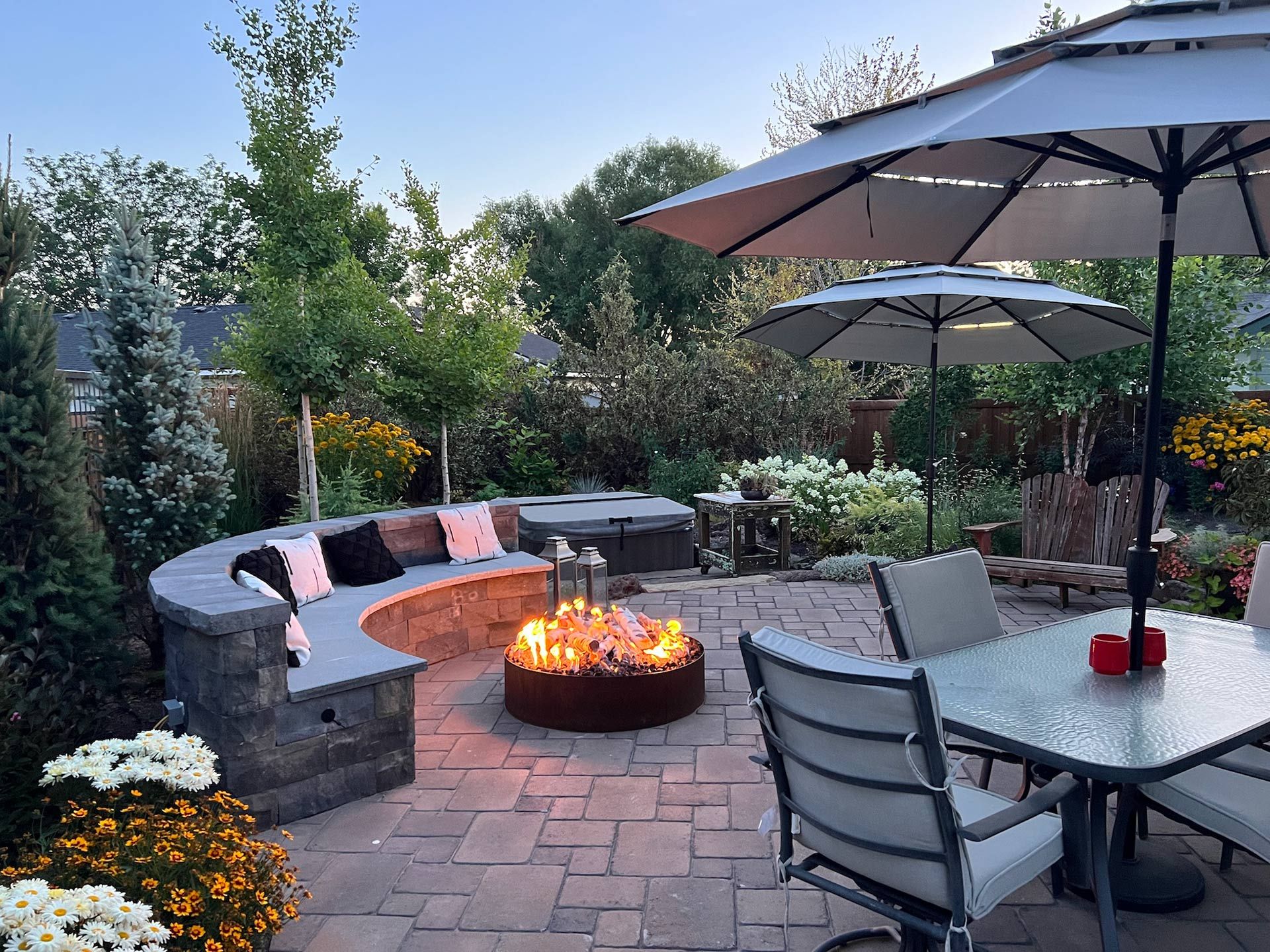 A patio with a fire pit , table , chairs and umbrellas