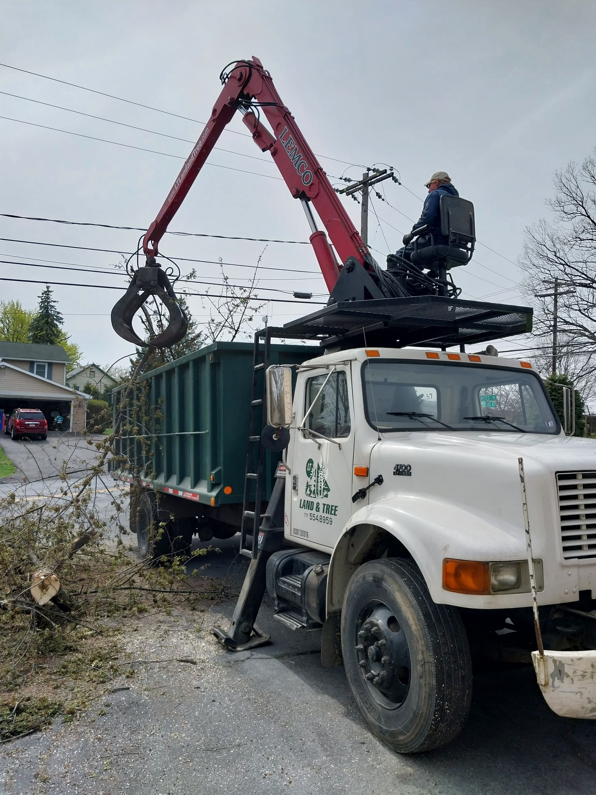 Bucket truck lifting branches beside a green dumpster on a residential street