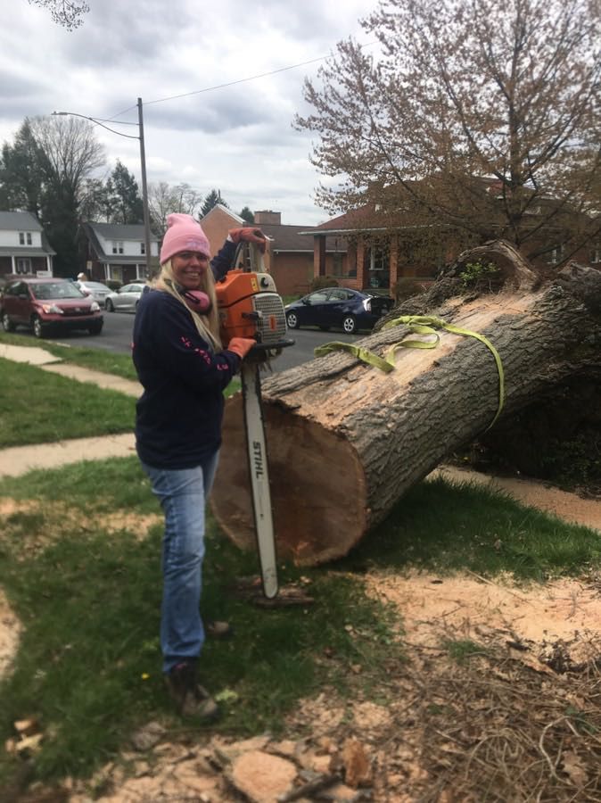 Woman operating a chainsaw next to a fallen tree trunk in a residential yard