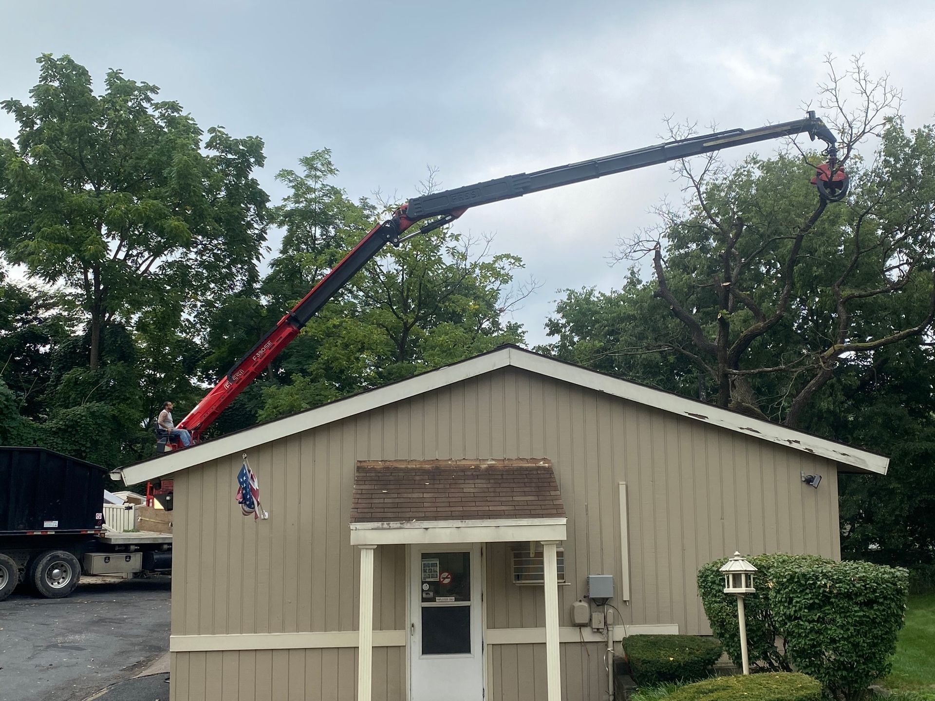 Crane lifting a large roof truss over a beige building with trees in the background