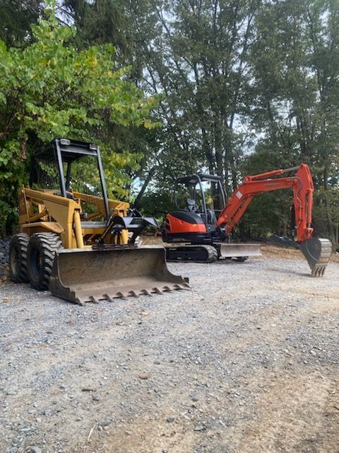 Yellow bulldozer and orange excavator parked on a gravel site with trees in the background