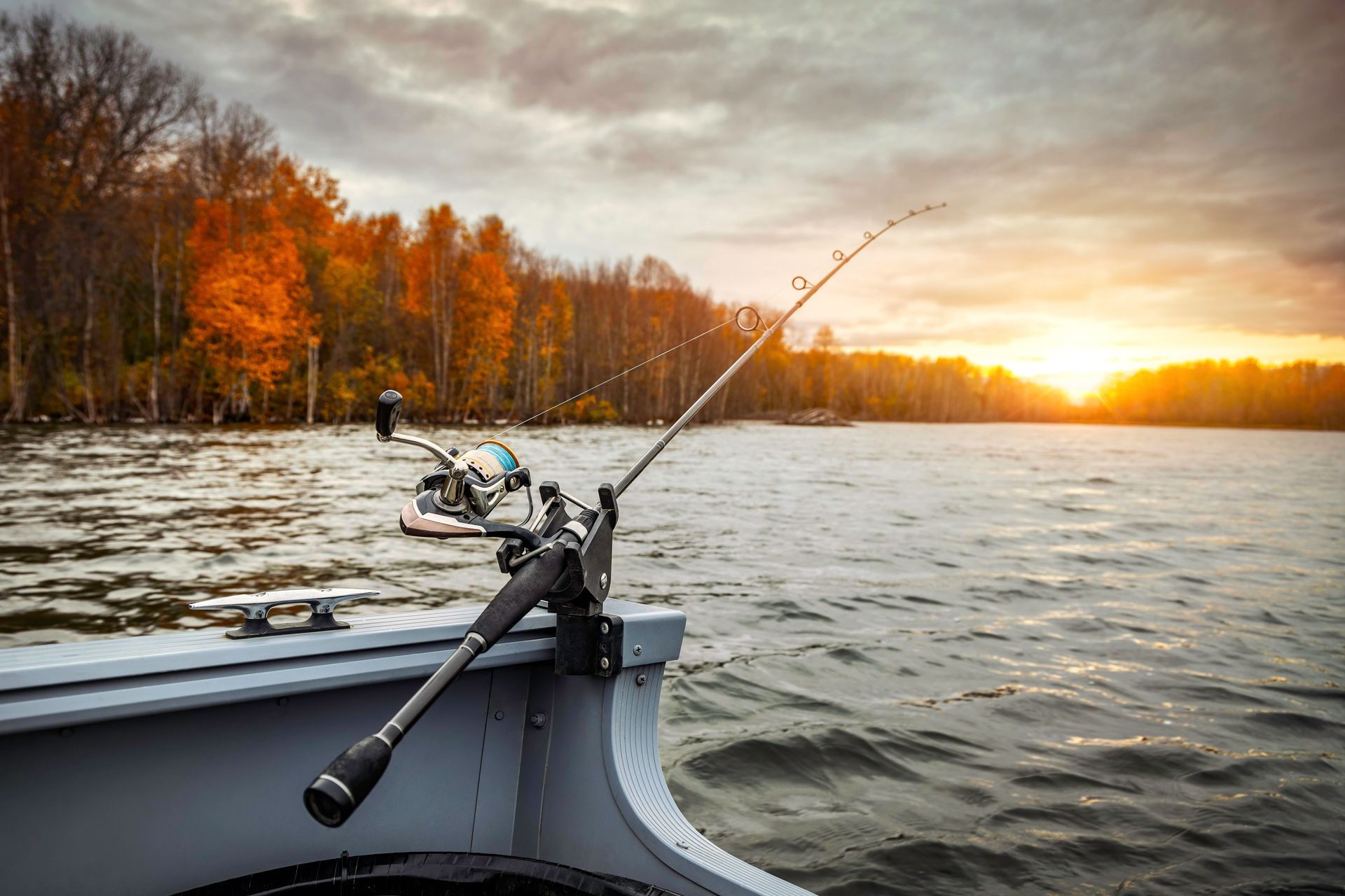 Boat fishing at sunset on a river, with autumn trees glowing along the shore.