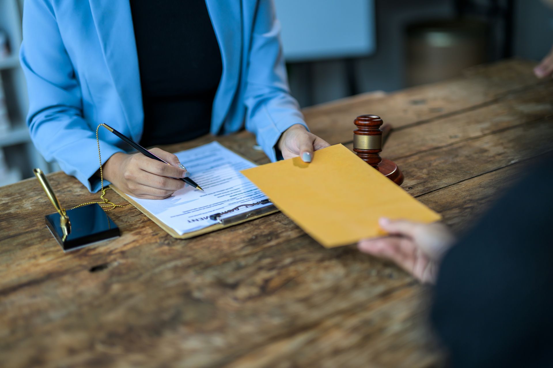 Business bankruptcy attorney in Cleveland, OH — Susan Lax Law Office Person signing documents at a wooden desk while another hands over a yellow envelope
