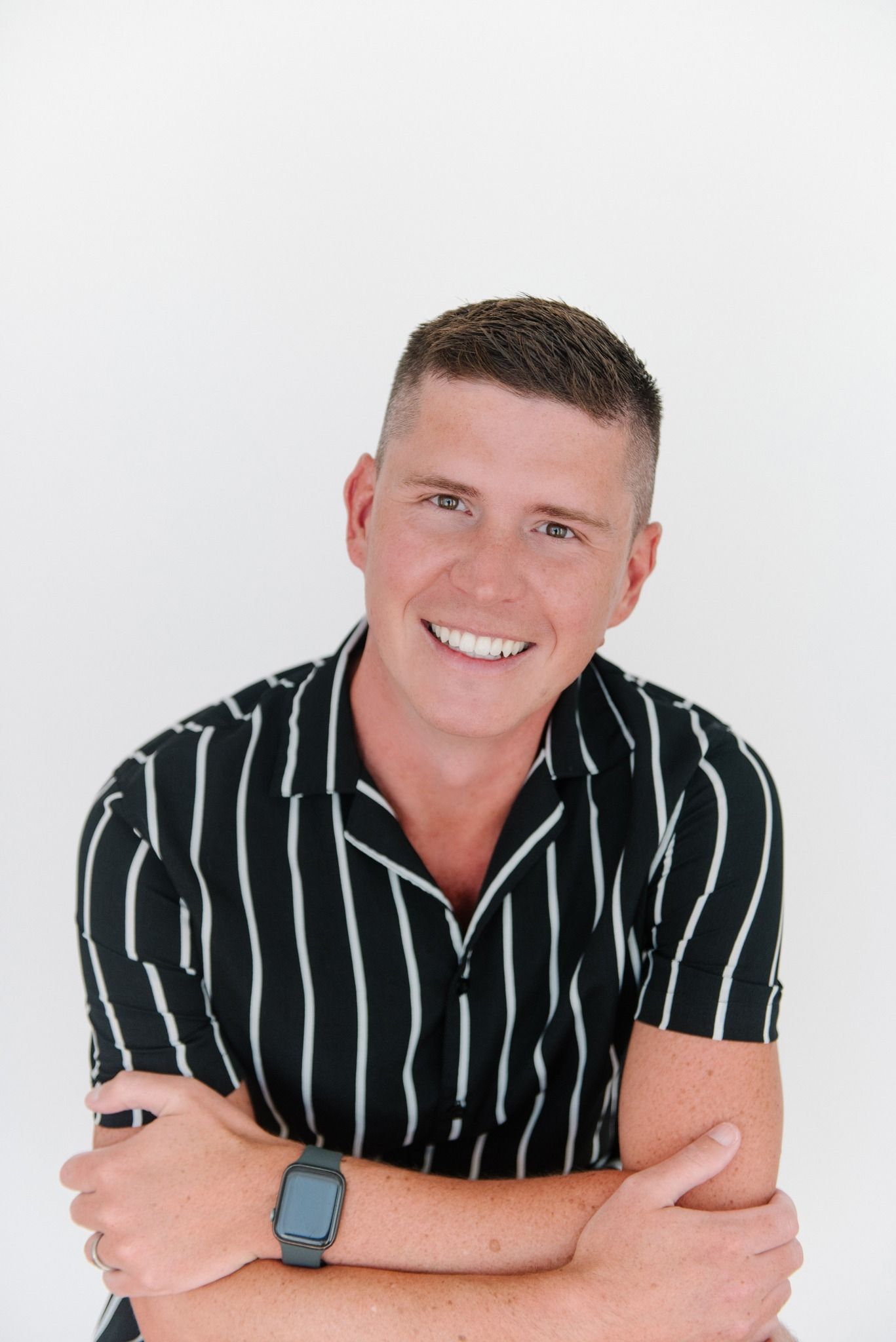 A man in a black and white striped shirt is smiling with his arms crossed