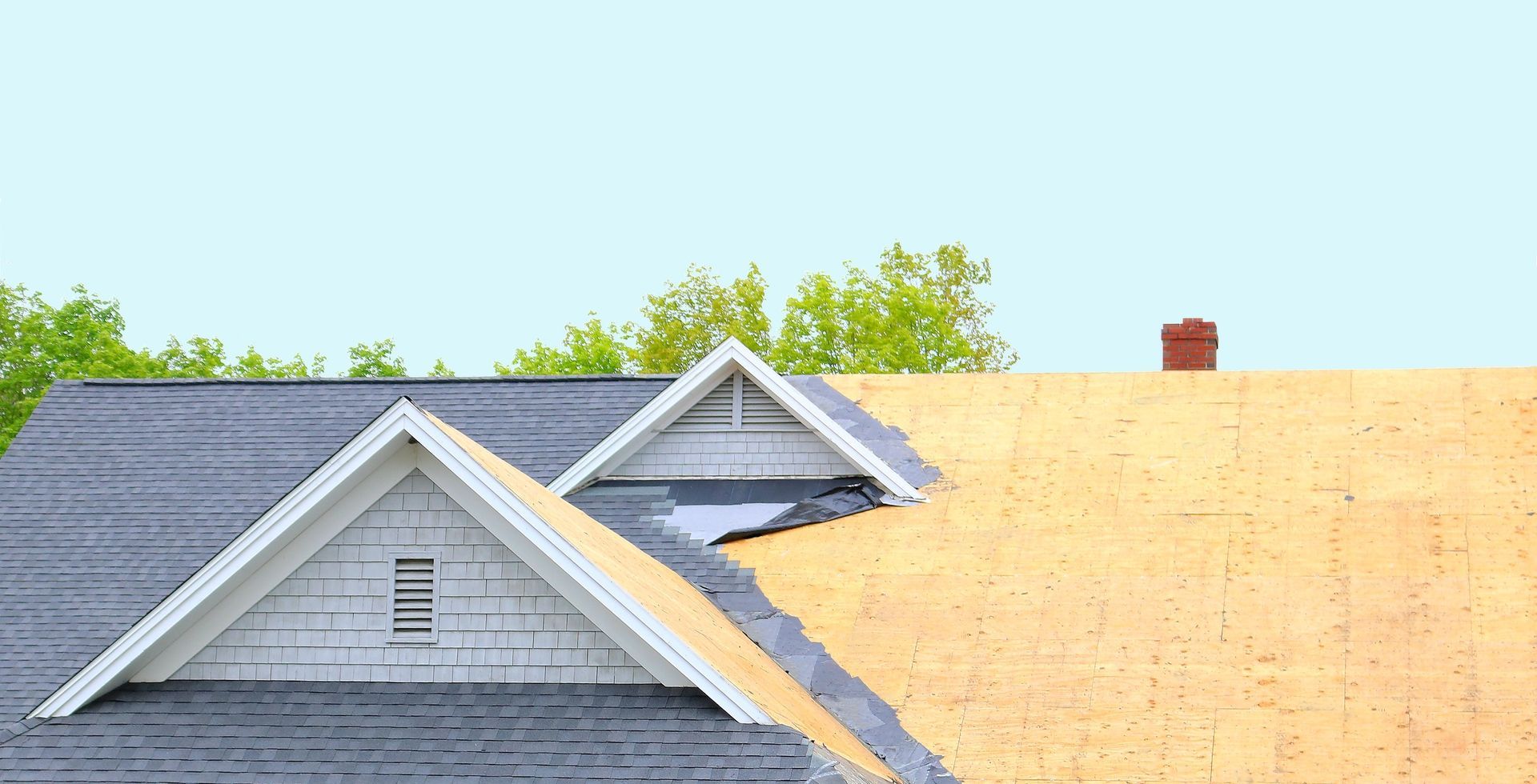 Un toit est en cours d'installation sur une maison avec une cheminée en arrière-plan.