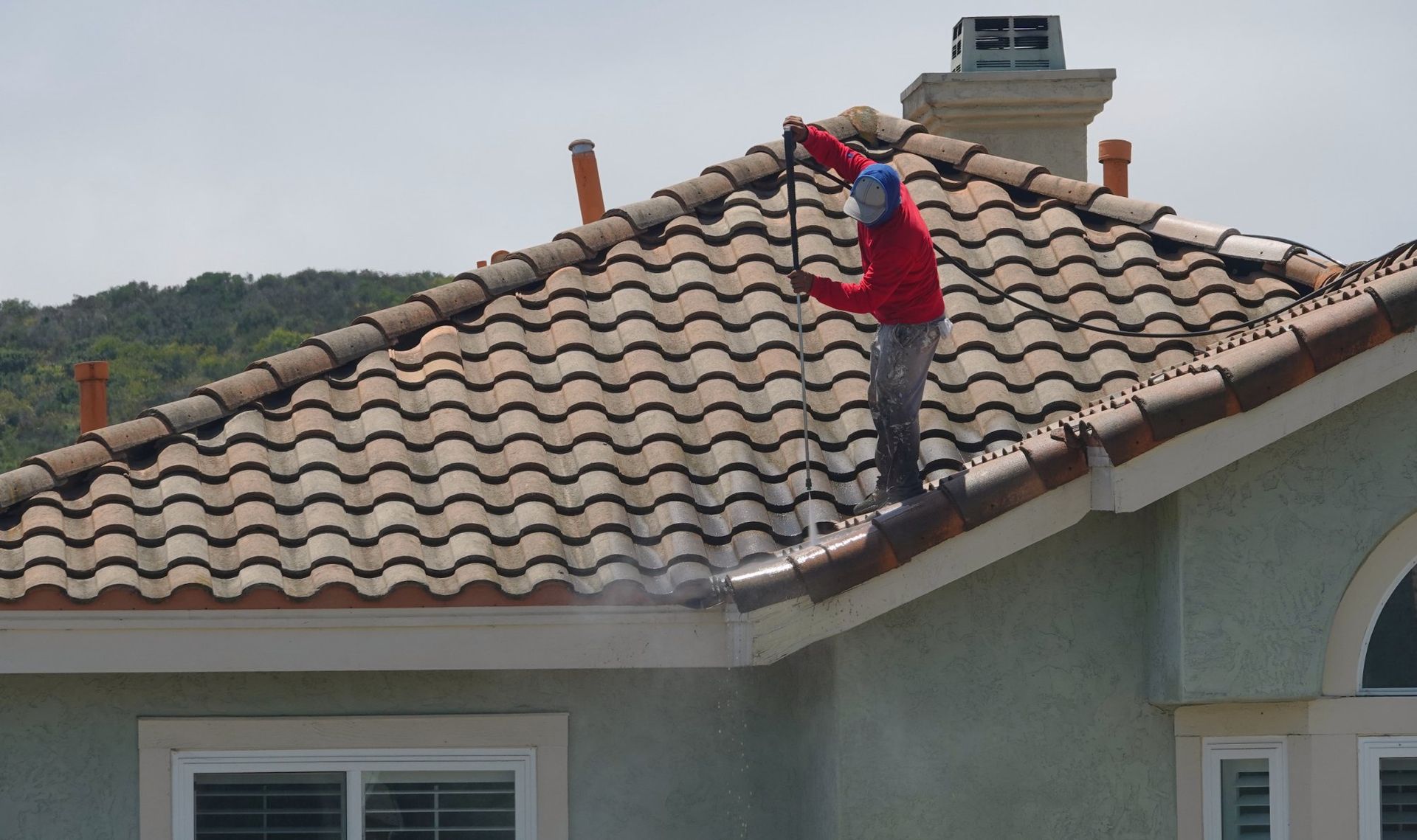 Person power washing a tiled roof.