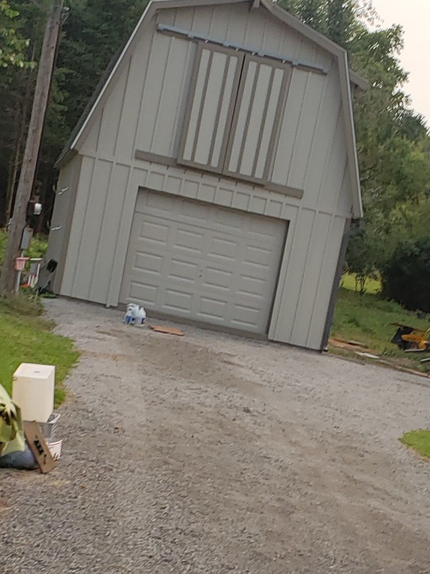 Person in white painting exterior window on beige house. Ladder visible, cloudy sky.