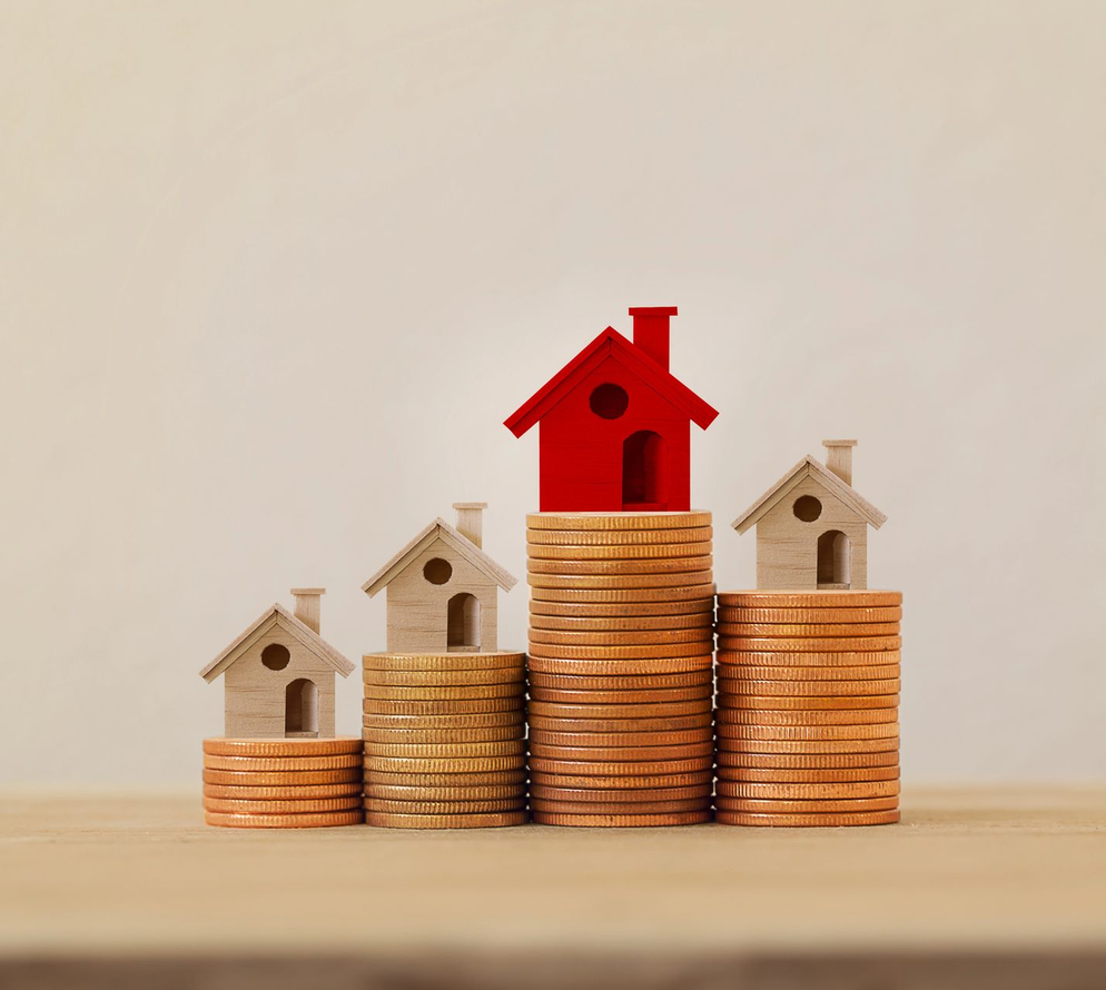 Mini casette su pile di monete, con una casa rossa in cima alla pila più alta, a simboleggiare l'investimento immobiliare.