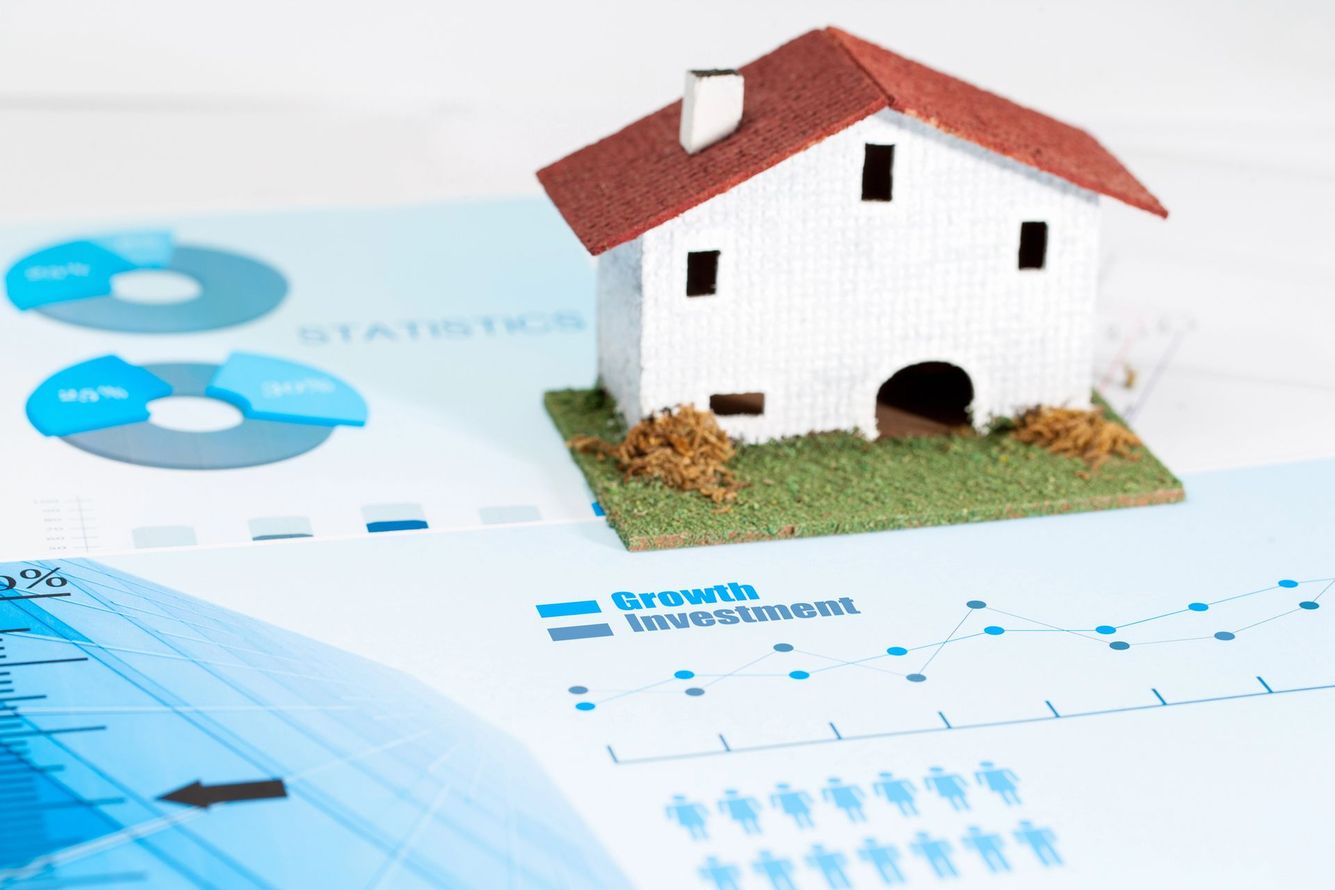 Una casa modello bianca su sfondi blu con grafici finanziari e pagine di calendario, a suggerire l'acquisto di una casa o la pianificazione immobiliare.