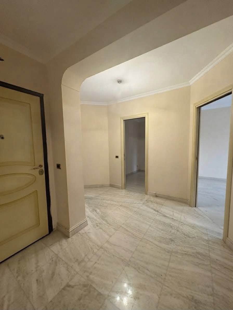 Corridoio vuoto color beige con pavimento in marmo, apertura ad arco e porte su entrambi i lati
