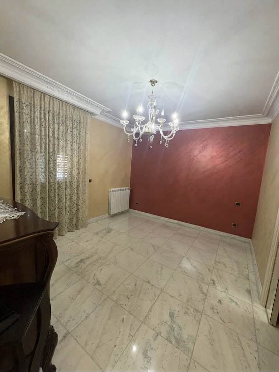 Stanza vuota con pavimento in marmo, lampadario, tende beige e una parete con un accento rosso.