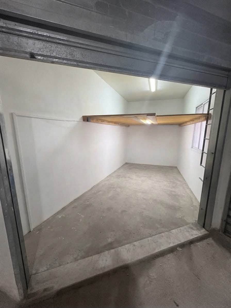 Stanza vuota in cemento con una bassa trave di legno sulla parete di fondo e un telaio di porta in metallo in primo piano.