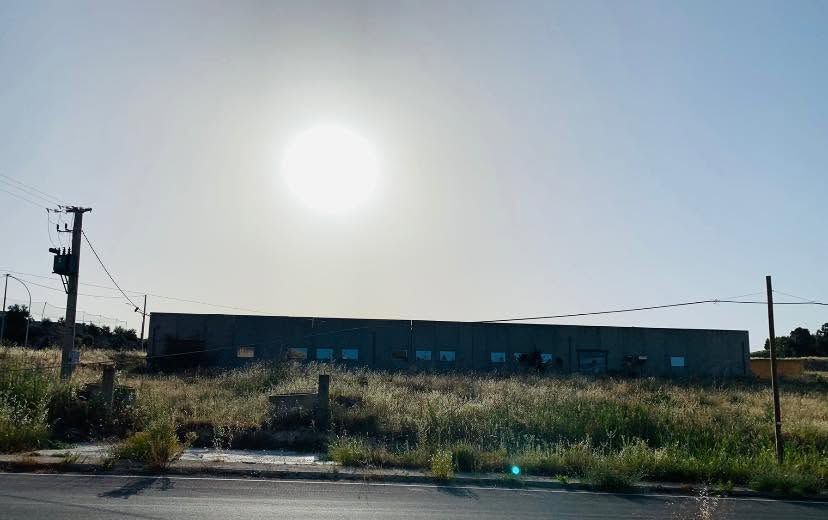 Lotto industriale vuoto e soleggiato con un lungo edificio basso ed erba incolta lungo il ciglio della strada.
