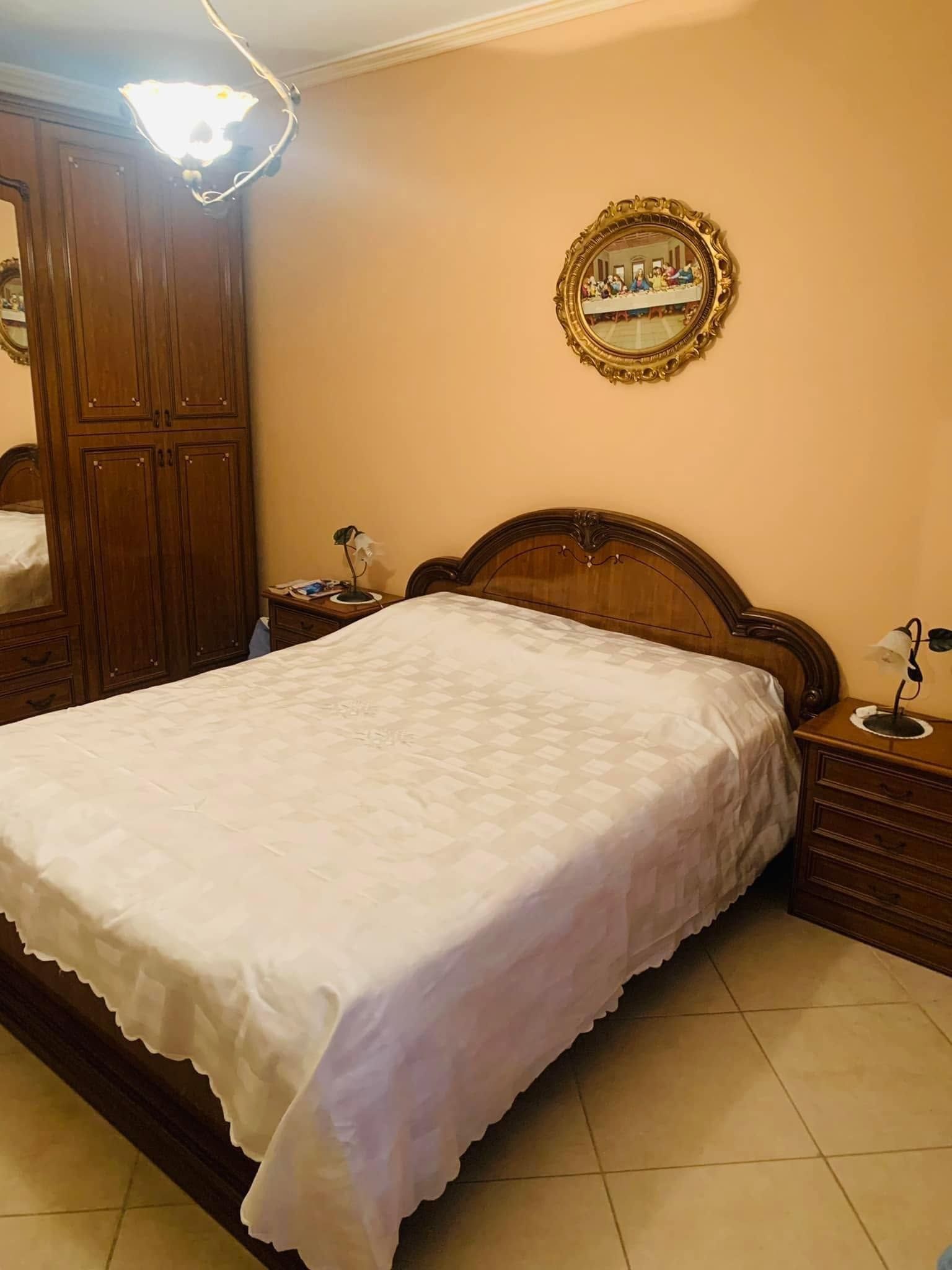 Camera da letto con letto ben rifatto, armadio in legno, comodini e specchio a parete con luce calda.