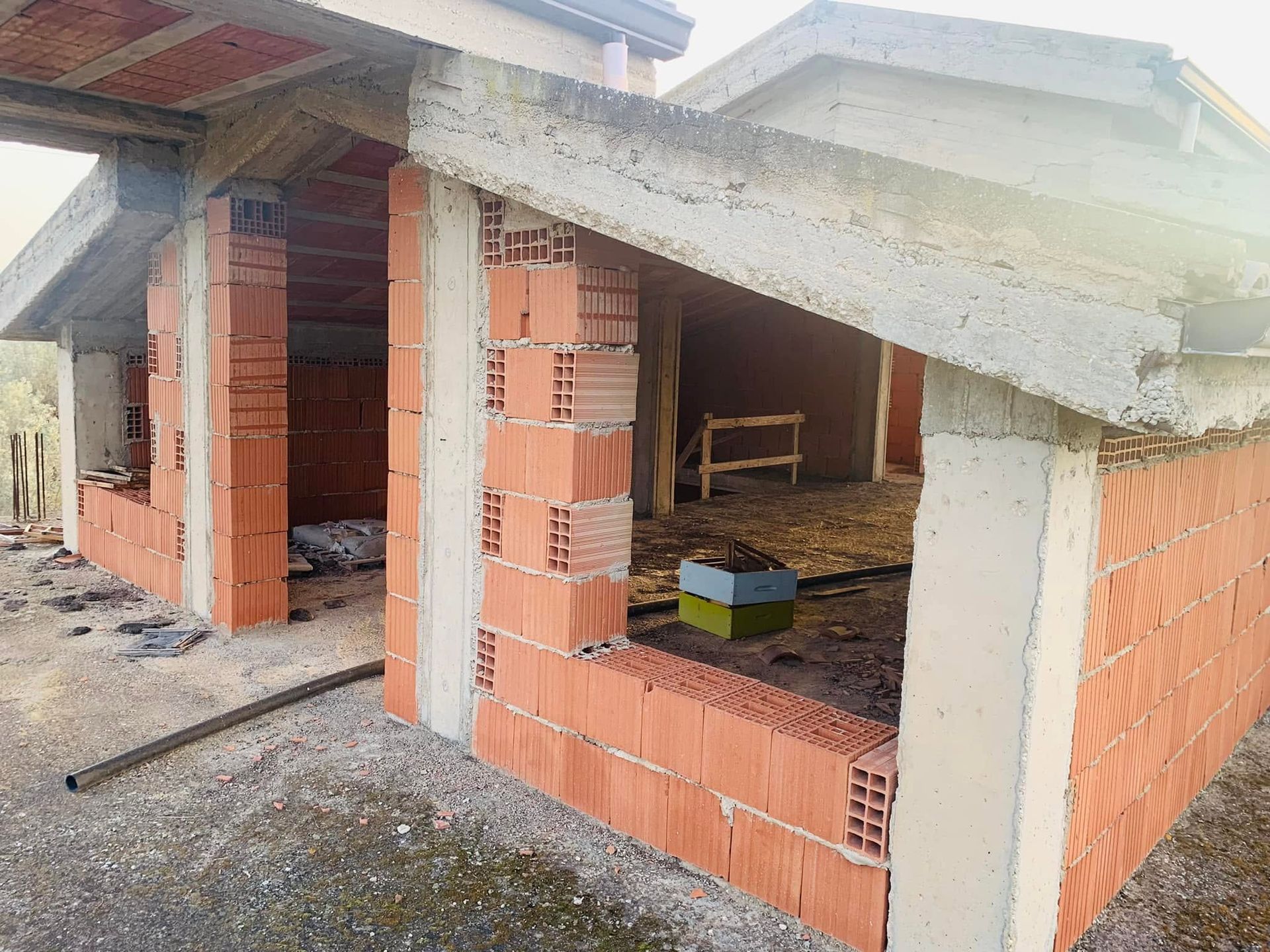Casa in mattoni non finita con tetto in cemento a vista, finestre aperte e materiali da costruzione all'interno.